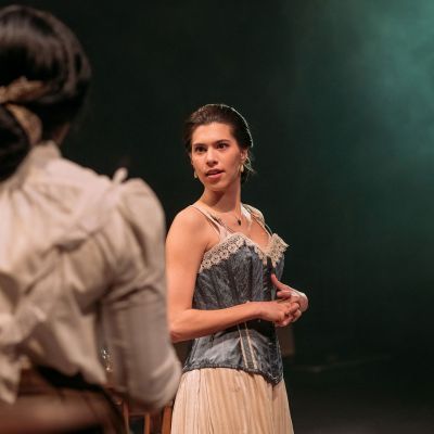 Two actors in period clothing and corsets perform on stage